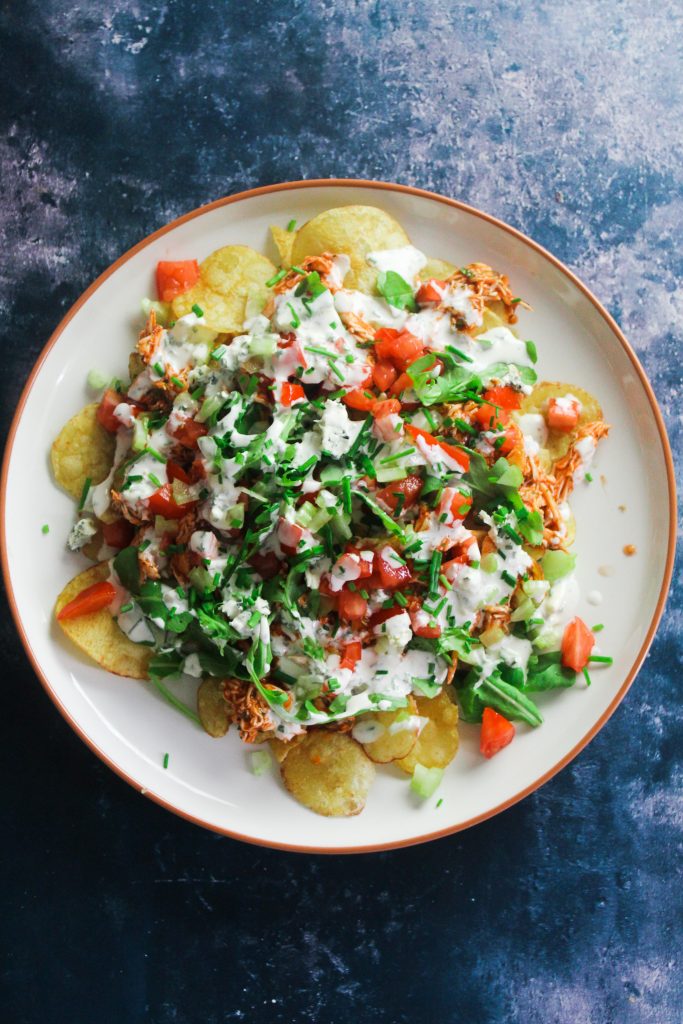 Plate of potato chips topped with buffalo shredded chicken, rocket, tomato, celery and blue cheese dressing 