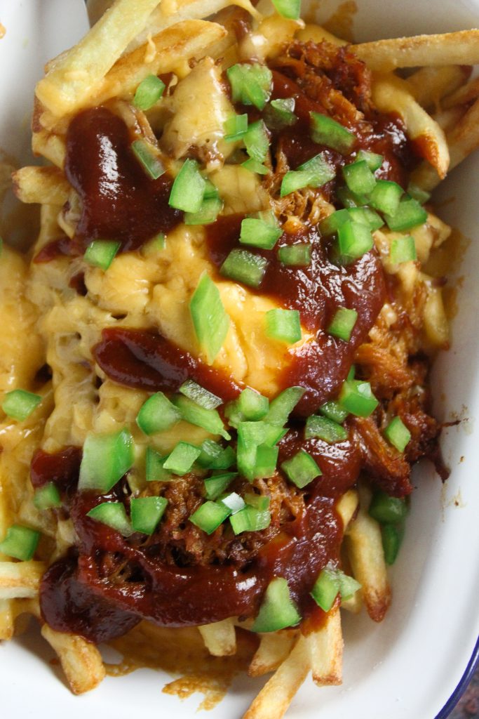 Close up of fries loaded with pulled pork, cheese, BBQ sauce and diced green pepper. 